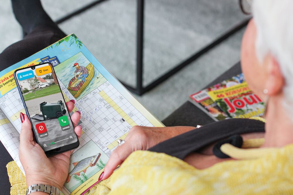 A close-up lifestyle shot of a person holding a smartphone showing a video call screen, with an open children's activity workbook and a magazine in the background.